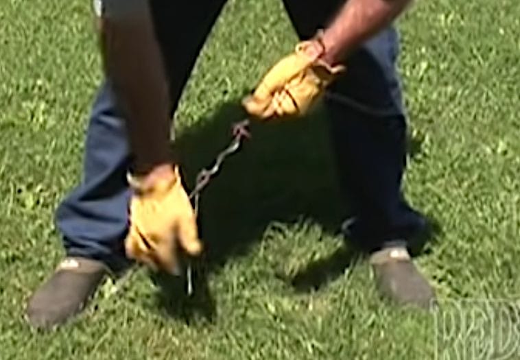 A man in yellow gloves carefully building a barbed wire fence in the grass