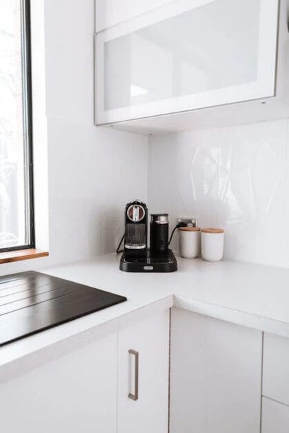 A white kitchen with a coffee maker plugged into an outlet near a window