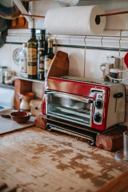 A red toaster on top of a wooden counter in a kitchen