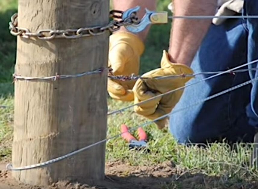A man in yellow gloves installing a barbed wire fence