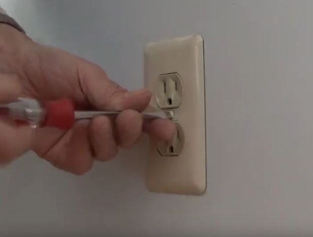 A person using a screwdriver to open an outlet on the wall