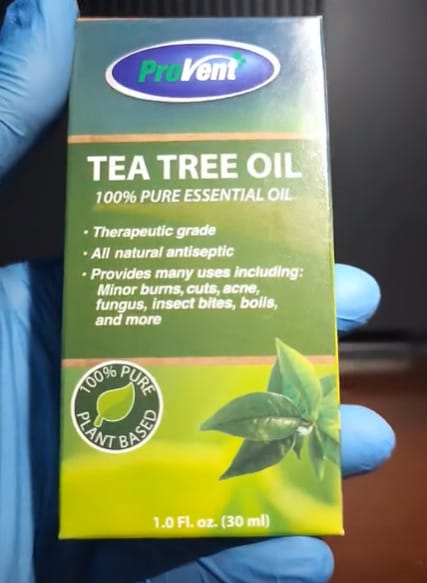 A person in blue gloves holding a box of tea tree oil