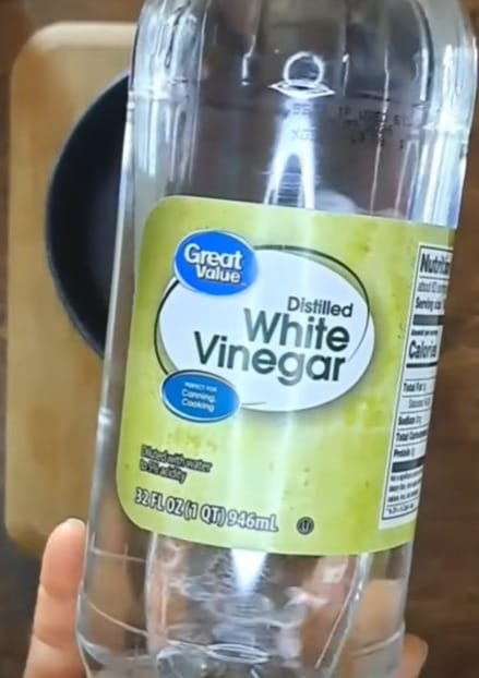 A person hiding an empty bottle of distilled white vinegar