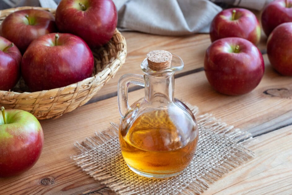 A group of apples in a basket and table with a bottle of apple cider