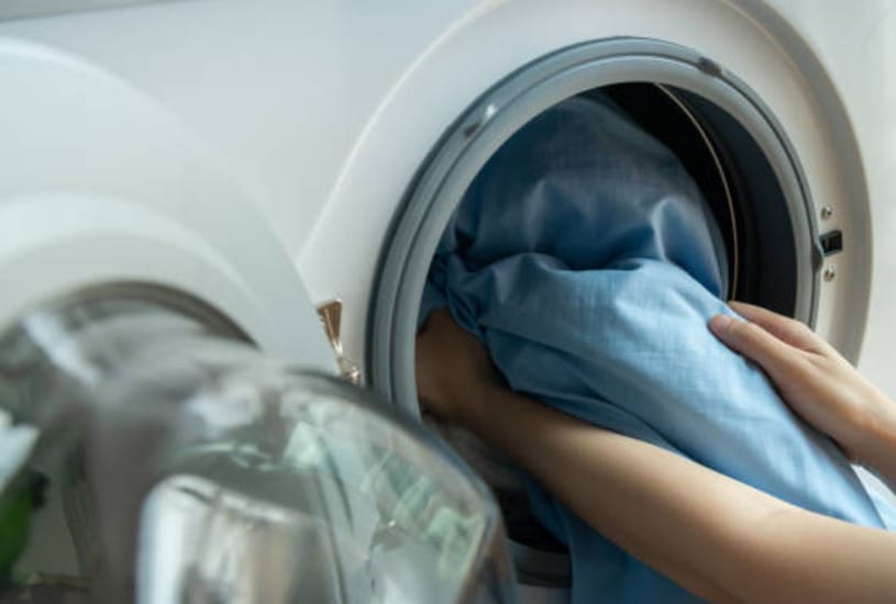 A woman is putting clothes into a washing machine