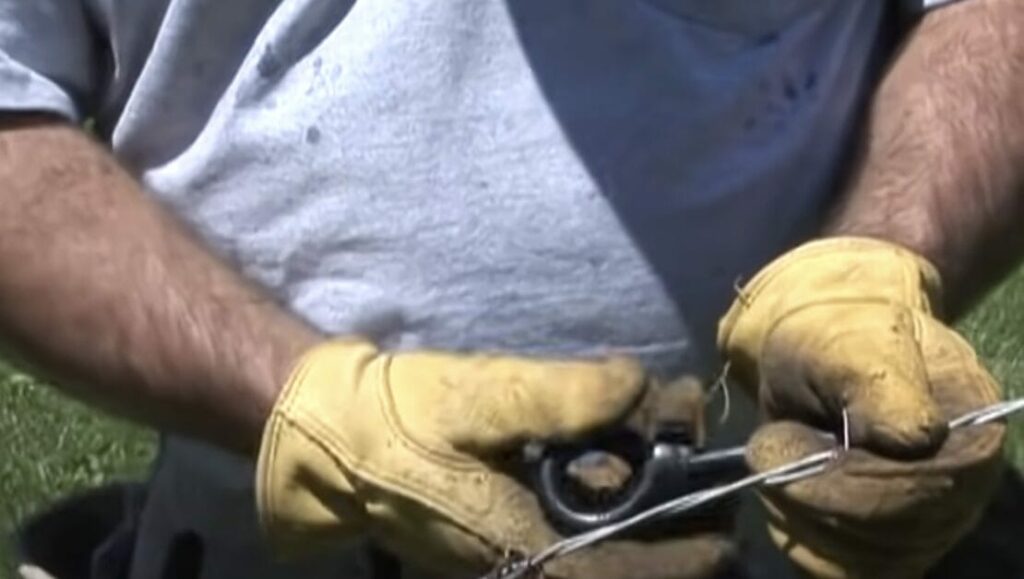 A person in yellow gloves uses a barbed wire gripper for additional safety