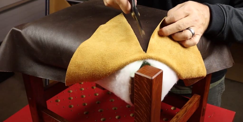 A person is cutting a leather fabric to fit on the chair