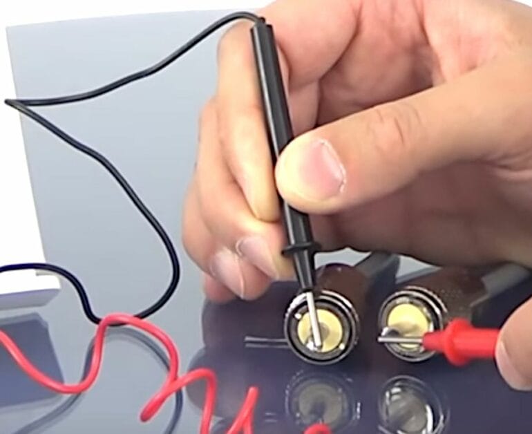 A person is using a wire to connect two batteries and test coax cable signal with a multimeter