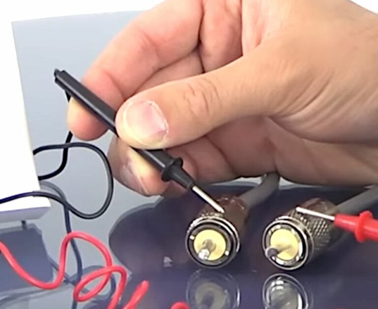 A person is using a wire to connect two wires together to test the coax cable signal with a multimeter