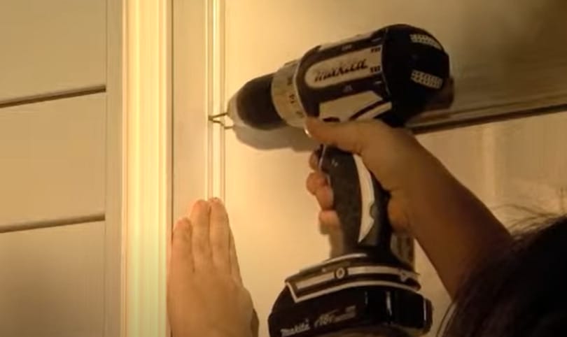 A man drilling the weatherstrip to secure it on the door