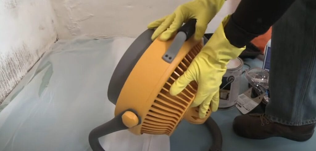A person wearing yellow gloves holding a box fan
