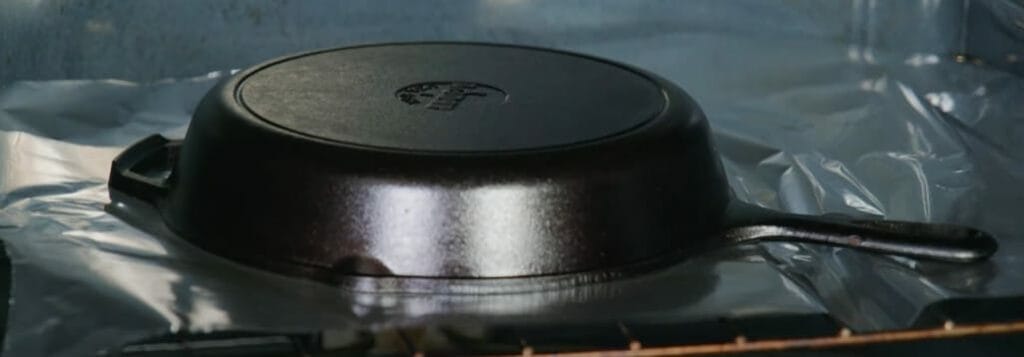 A cast iron pan sitting at the top of a rack tray with aluminum foil