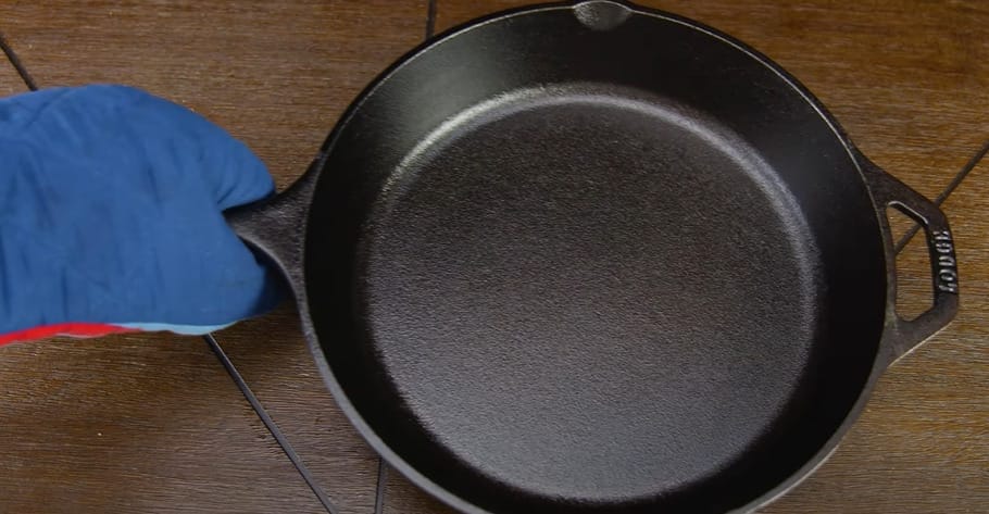 A person wearing a blue gloves and holding an iron cast pan
