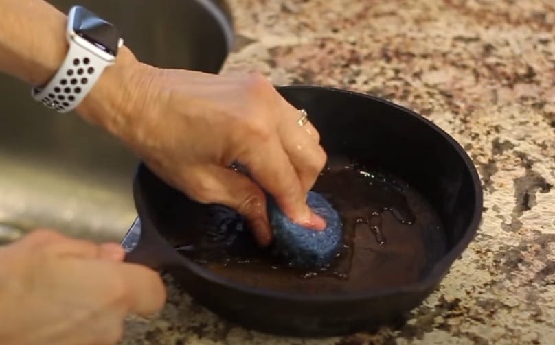 A person scrubbing the pan with a fine steel wool