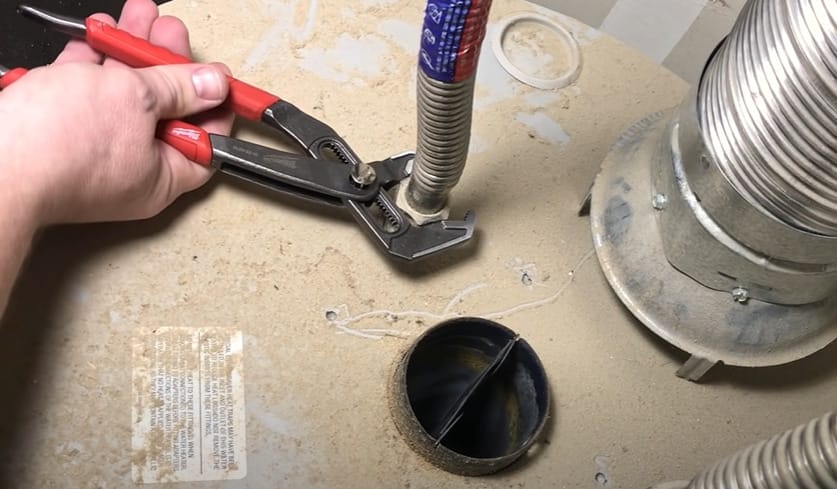 A person is using pliers to remove a pipe from a sink during a repair