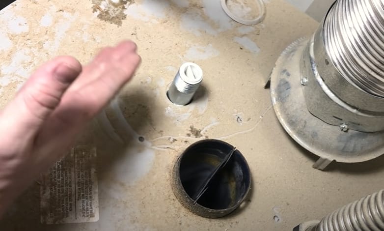A person's hand reaching into a sink drain to repair a water heater