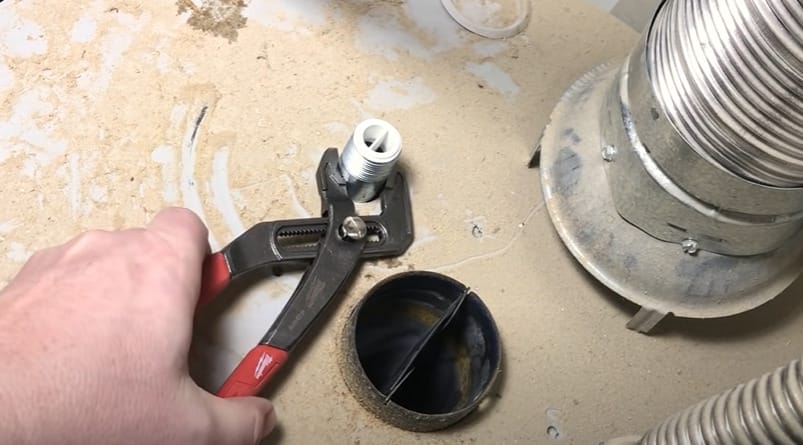 A person is using pliers to repair a pipe connected to a water heater