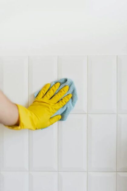 A person wearing yellow gloves tackles cleaning a tiled wall