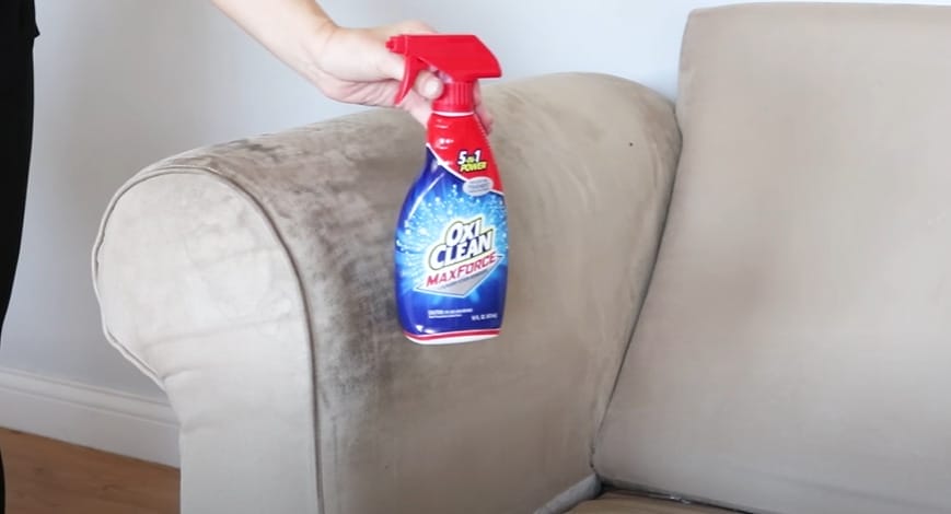 A person holding a spray bottle of OXL CLEAN to clean a couch