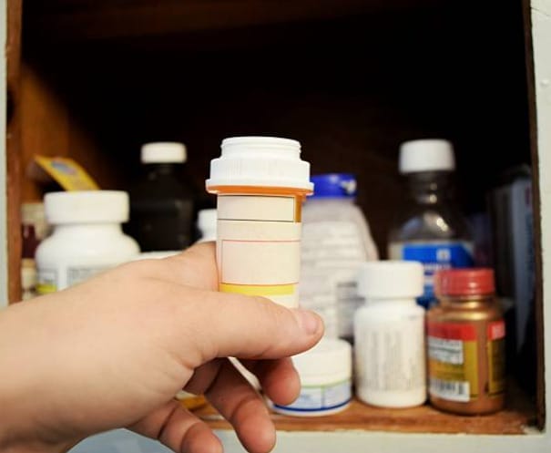 A person holding a pill bottle with other pill bottles on the background