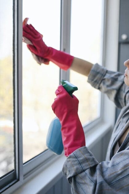 A woman in pink gloves cleaning a window with spray cleaner and cloth