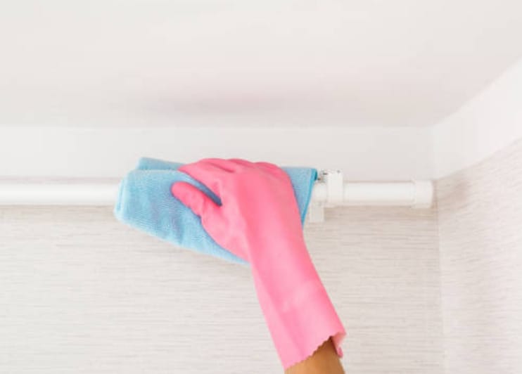 A woman in pink gloves cleaning the top bar of a bathroom with a blue clothe