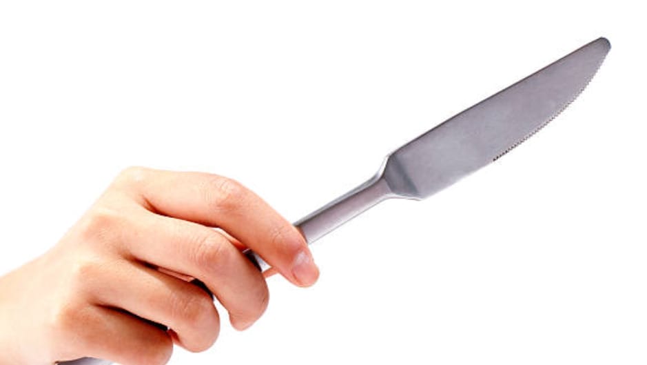 A person holding a butter knife in a white background