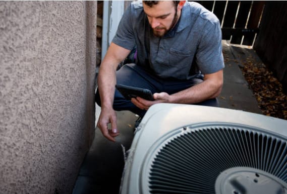 A man inspecting an air conditioning unit for possible AC capacitor replacement