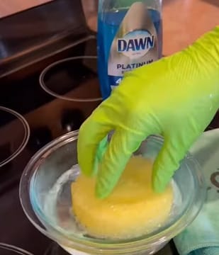 A person wearing a neon green gloves soaking a sponge on a bowl of water solution