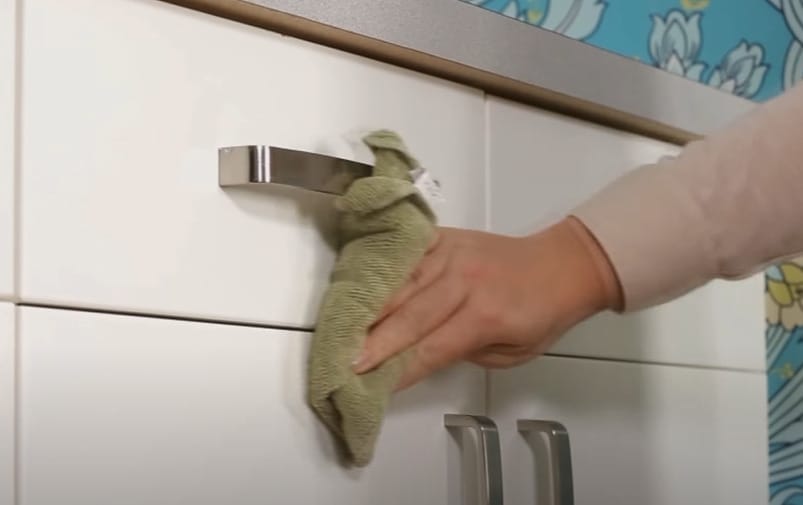 A person removing grease from kitchen cabinets with a cloth