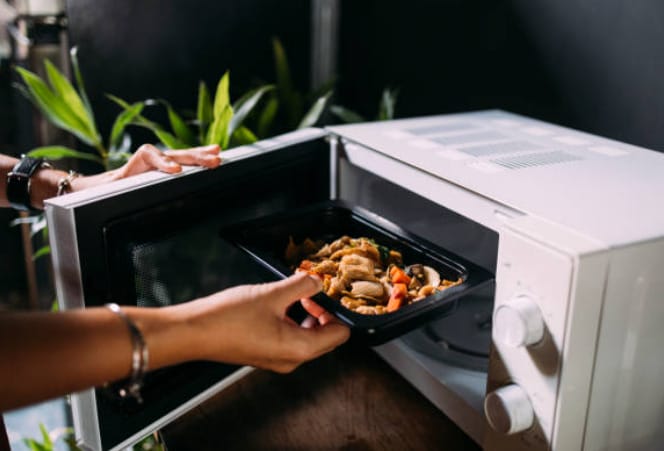A person putting food on the microwave oven