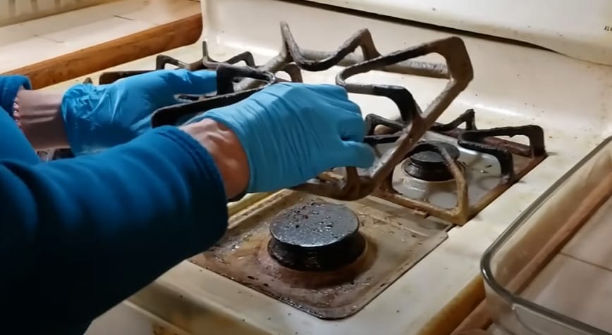 A person in blue gloves cleaning the stove