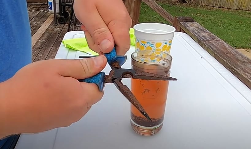 A person holding the plier beside a glass of rusty water