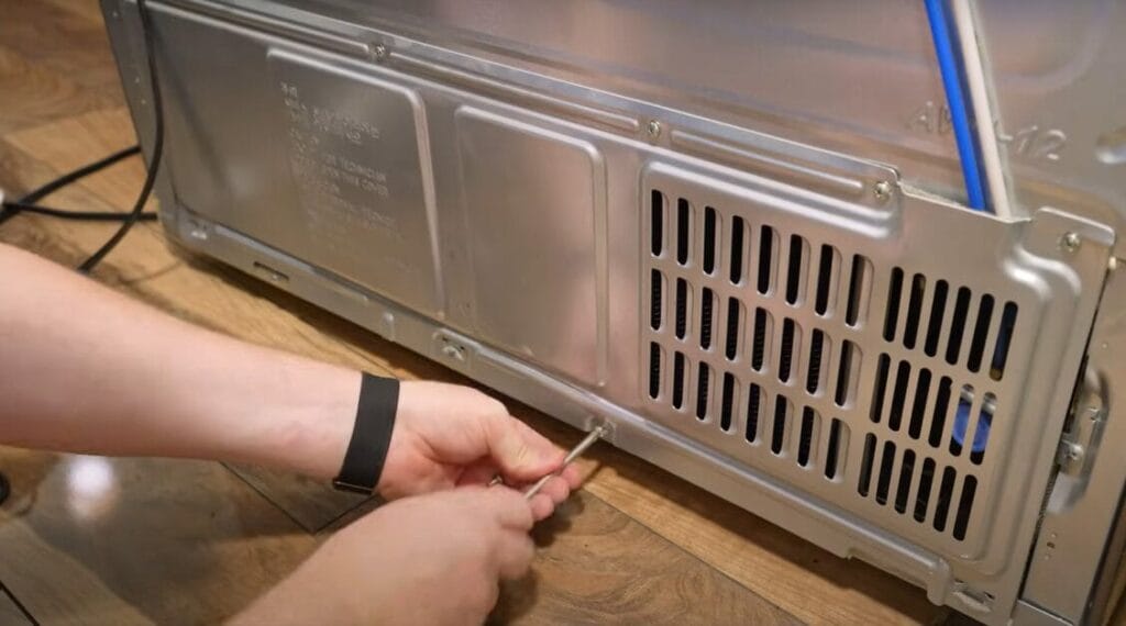 A person is putting screws into a refrigerator's back panel