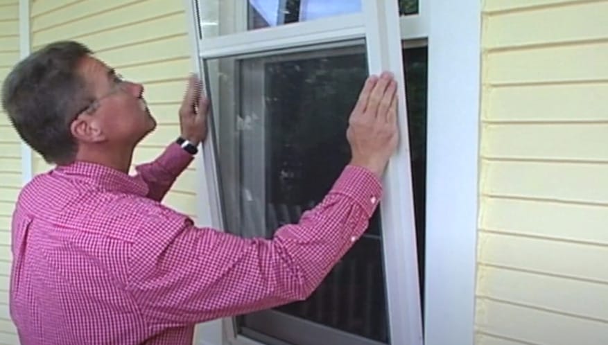 A man in pink checkered polo installing a glass with frame on a window