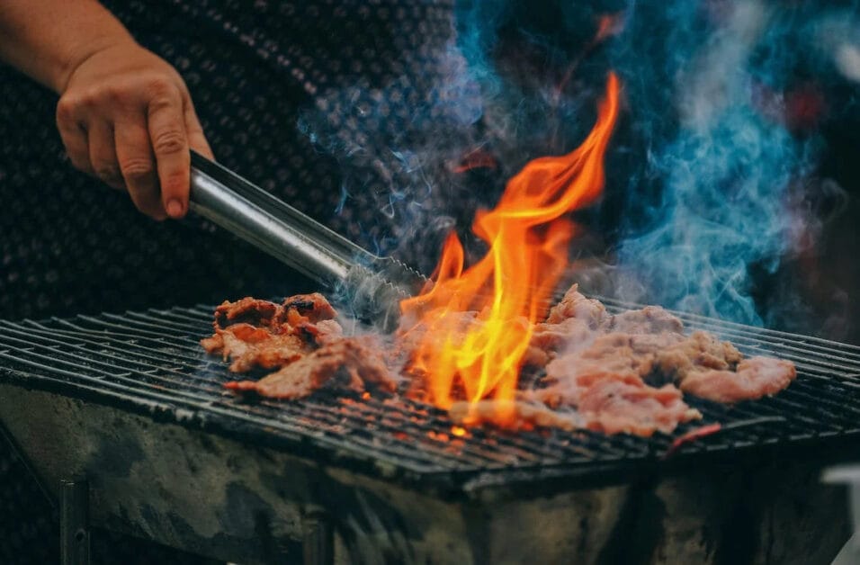 A person grilling a barbecue with fire