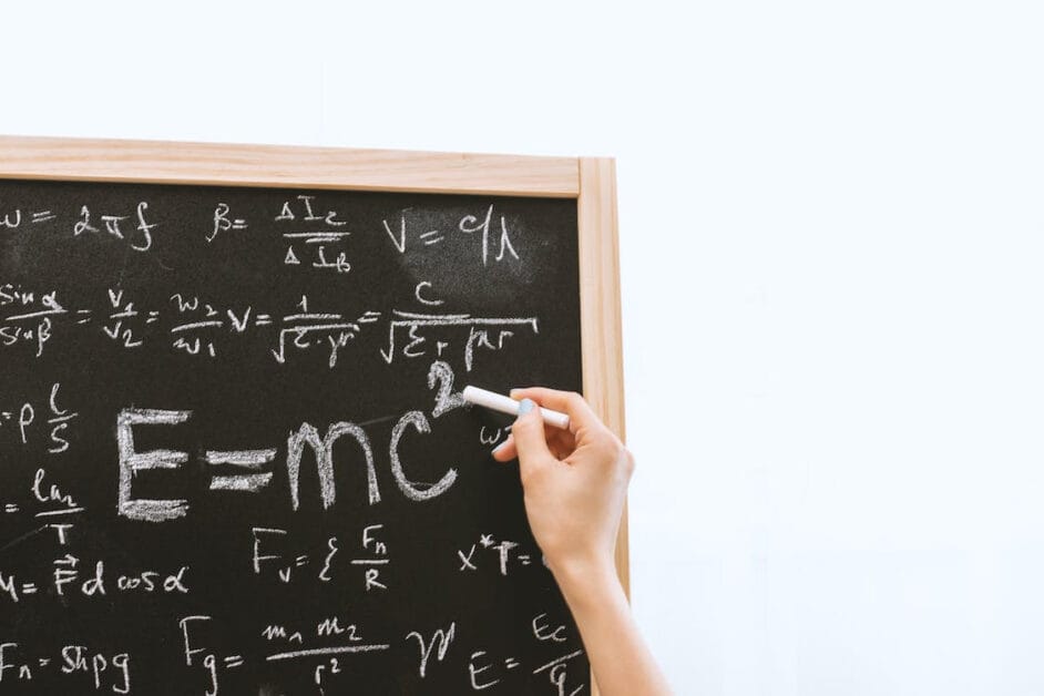 A person writing on a blackboard with formulas on it