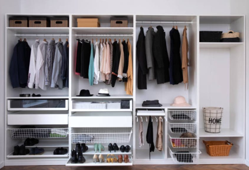 A white closet packed with clothes, shoes, and baskets