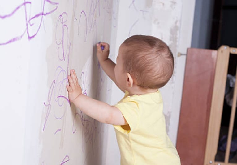 A baby is drawing on a white wall