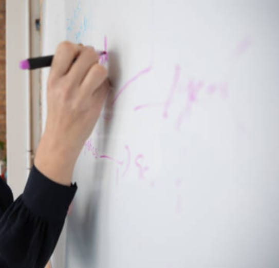 A woman  writes on a whiteboard with pink pen