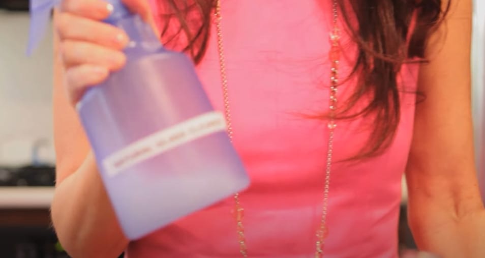 A woman is holding a homemade cleaning mixture purple bottle