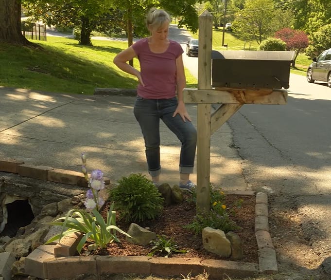 A woman DIYing her landscaping projects in the yard next to a mailbox