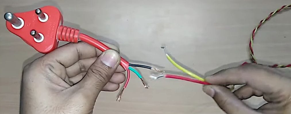 A person is holding a red wire and a 3 prong plug