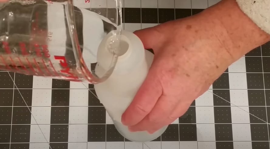 A person DIY-ing homemade window cleaner by pouring water into a bottle