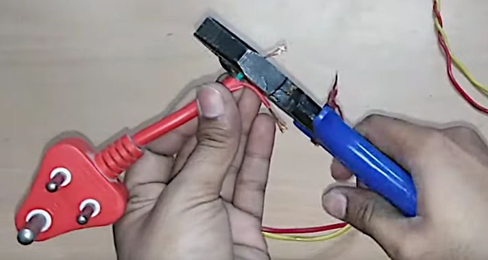 A person using a plier to carefully cut wires of a 3-prong plug