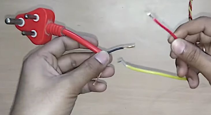 Two hands holding two wires on a table, demonstrating how to wire a 3 prong plug
