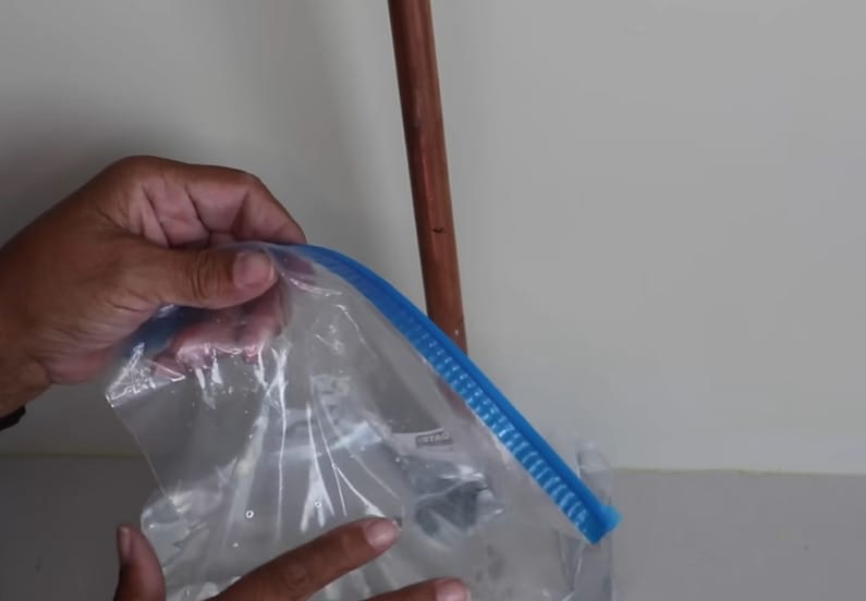 A person holding a plastic bag of hot water to be put on the water pipe
