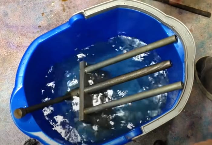 A blue bucket filled with water and metal rods used to remove rust from kitchen ingredients