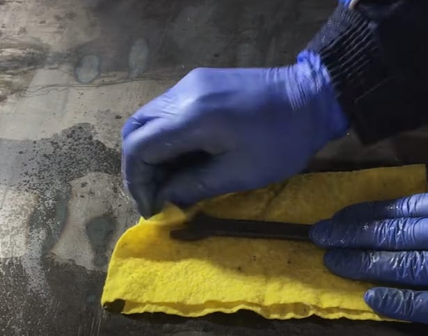 A person in blue gloves is using a yellow cloth to clean a piece of metal and remove rust