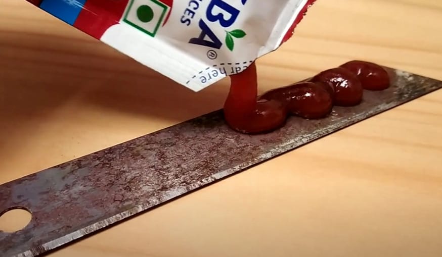 A person putting a portion of ketchup to a rusted metal